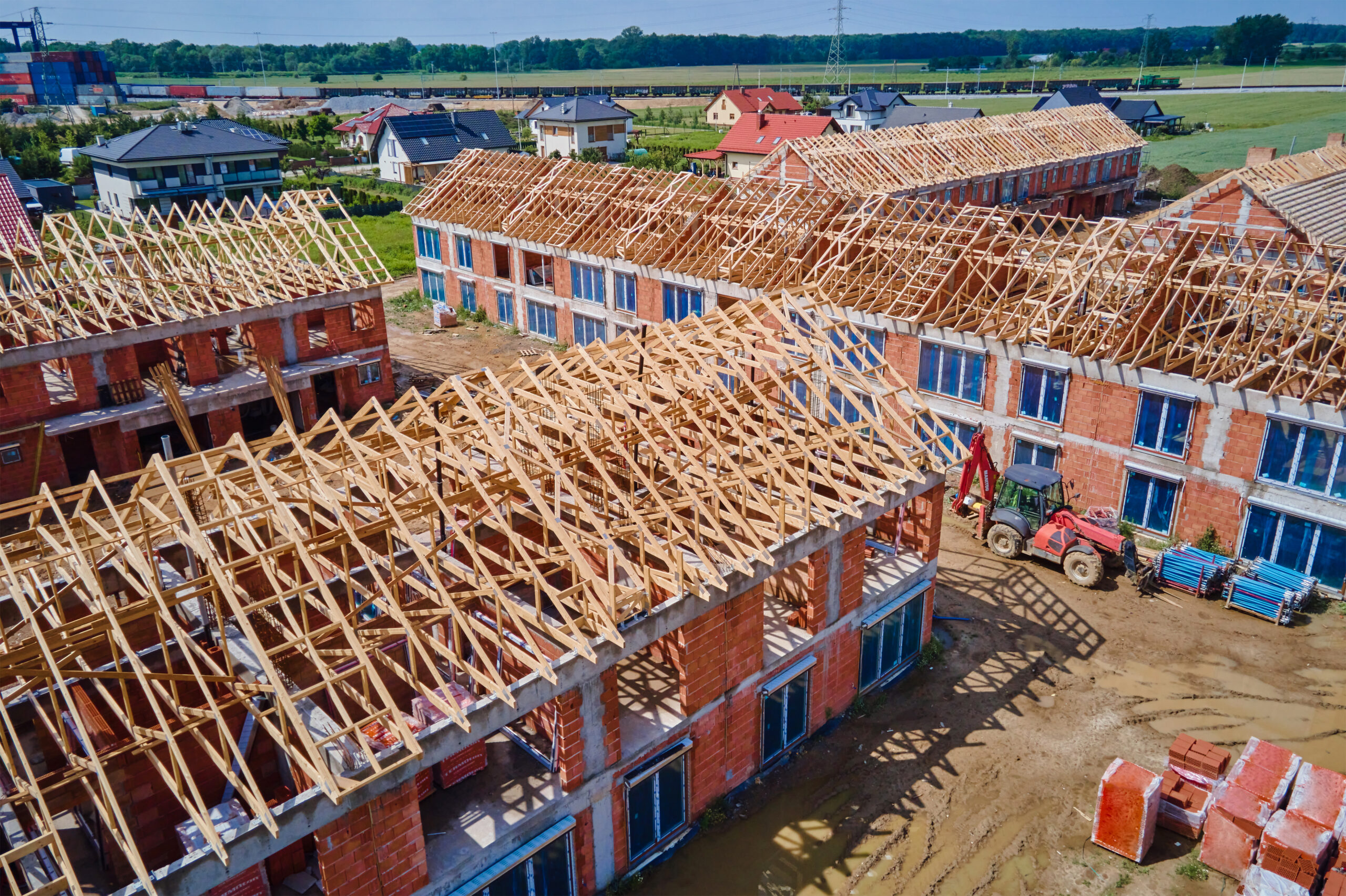 Aerial view of new house construction project in suburban area. Residential building wooden roof frame with truss, post and beams at construction site. Manufacture of new neighborhood in small town